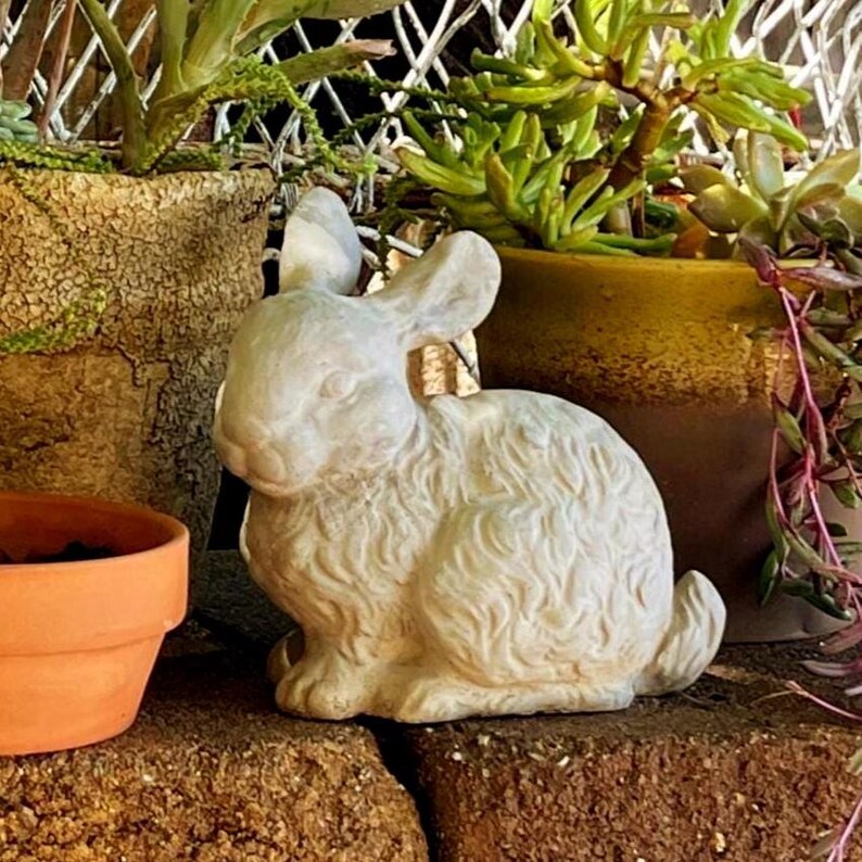 May include: A white, textured rabbit figurine in a seated position with upright ears and detailed fur markings. The sculpture is crafted with a matte finish and displays a realistic posture, capturing the form of a small hare in a neutral tone.