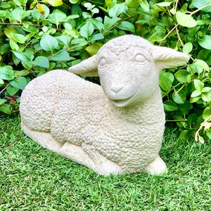 May include: A white concrete sculpture of a lamb lying down with its head turned to the side. The lamb has a detailed, textured surface that resembles wool.