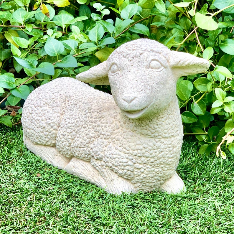 May include: A white concrete sculpture of a lamb lying down with its head turned to the side. The lamb has a detailed, textured surface that resembles wool.