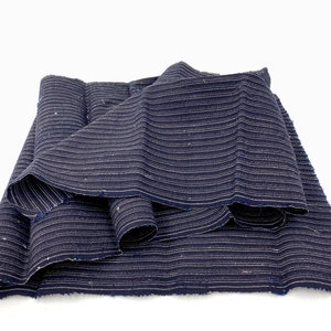 May include: A folded piece of dark blue fabric with horizontal white stripes. The fabric is layered, showing the texture and pattern. The edges appear to be unfinished, adding to the rustic aesthetic. The fabric is likely used for clothing or home decor.