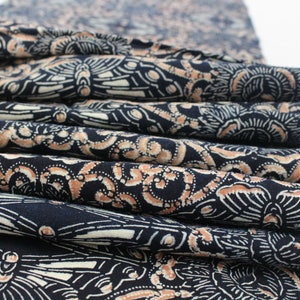May include: A stack of folded fabric with a repeating pattern of white and tan designs on a navy blue background. The fabric appears to be cotton or a similar material, with visible folds and edges.