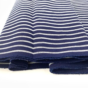 May include: Close-up of a navy blue and white striped fabric. The fabric is folded and has a raw edge.