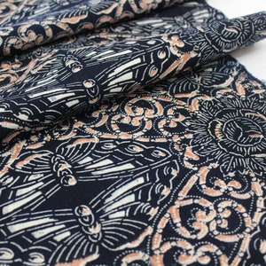 May include: Dark blue fabric with a repeating pattern of butterflies, floral designs, and swirls in white and peach. The fabric is folded, showing the detailed print and texture. Ideal for sewing projects.