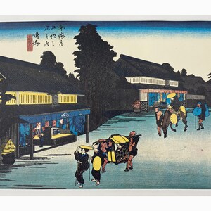 May include: A woodblock print depicting a street scene in Japan. The print features a group of people walking along a street lined with buildings. The people are wearing traditional Japanese clothing and carrying umbrellas. The print is in shades of blue, green, yellow, and black.