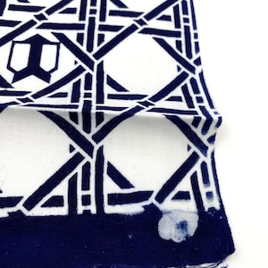 May include: A white fabric with a navy blue geometric pattern. The fabric has a frayed edge.