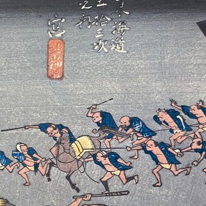 May include: Japanese woodblock print showing a procession of figures, some on foot and others on horseback, against a grey backdrop. The figures are dressed in blue and white clothing. Japanese text is visible in the upper left.