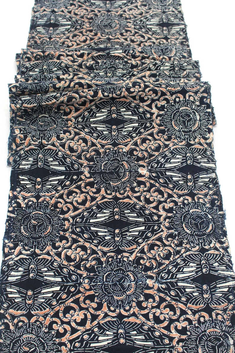 May include: Folded fabric with a repeating pattern of stylized butterflies, flowers, and swirling lines in black, white, and peach. The fabric is likely cotton or a similar material, and the design is printed on the surface.