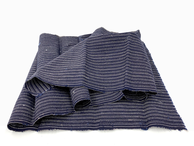 May include: A folded piece of dark blue fabric with horizontal white stripes. The fabric is layered, showing the texture and pattern. The edges appear to be unfinished, adding to the rustic aesthetic. The fabric is likely used for clothing or home decor.