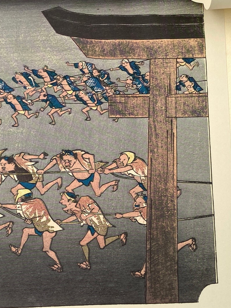 May include: A woodblock print showing figures pulling ropes, set against a muted grey backdrop. The people are dressed in traditional Japanese attire, with some wearing blue jackets and others patterned garments. The print has a historical feel.