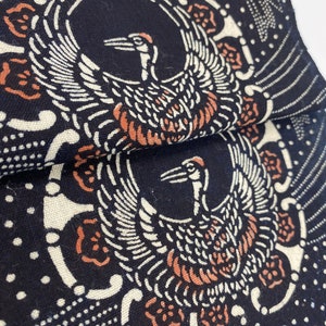 Puede incluir: Tela negra con un dise&ntilde;o blanco y naranja de dos grullas con las alas extendidas. La tela tiene un patr&oacute;n repetitivo de peque&ntilde;os puntos blancos.