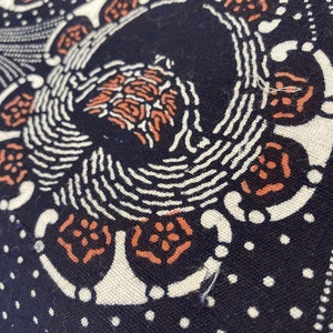 Puede incluir: Primer plano de una tela negra con un dise&ntilde;o estampado en blanco y naranja. El patr&oacute;n presenta un motivo repetitivo de c&iacute;rculos y espirales.