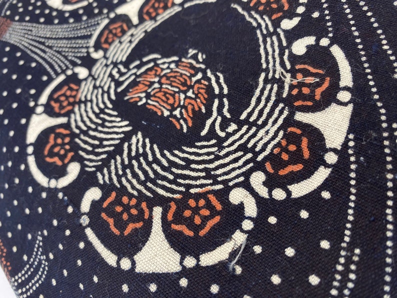 Puede incluir: Primer plano de una tela negra con un dise&ntilde;o estampado en blanco y naranja. El patr&oacute;n presenta un motivo repetitivo de c&iacute;rculos y espirales.