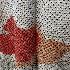 May include: Close-up of a white fabric with a black polka dot pattern. The fabric has a textured surface and is folded in the center. The fabric is decorated with a red and orange floral design.