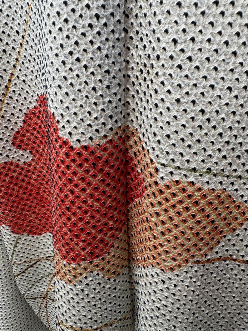 May include: Close-up of a white fabric with a black polka dot pattern. The fabric has a textured surface and is folded in the center. The fabric is decorated with a red and orange floral design.