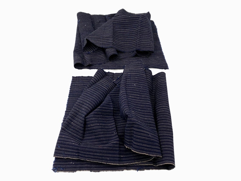 May include: Several pieces of navy blue fabric with a subtle striped pattern. The fabric is rolled and folded, showcasing its texture and potential for various sewing projects. The fabric appears to be a medium weight.