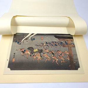 May include: A Japanese woodblock print showing a group of people running, pulling a horse-drawn cart. The print features a dark, stormy sky and traditional Japanese architecture. The print is framed by a cream-coloured mount.