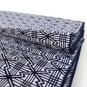 May include: A folded fabric with a geometric pattern in shades of white and navy blue. The fabric has a repeating pattern of interlocking squares and triangles.