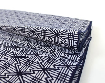 May include: A folded fabric with a geometric pattern in shades of white and navy blue. The fabric has a repeating pattern of interlocking squares and triangles.
