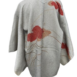 May include: A white Japanese kimono with a red and orange floral pattern. The kimono has a textured fabric and a traditional collar.