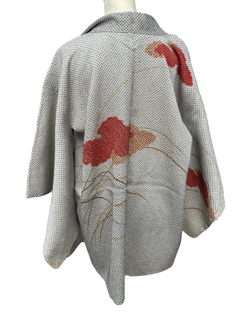 May include: A white Japanese kimono with a red and orange floral pattern. The kimono has a textured fabric and a traditional collar.