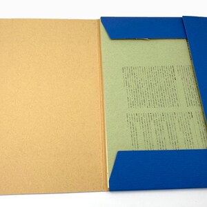 May include: An open file folder with a tan cover and a blue spine. Inside, a light green paper holds printed text. The folder is secured with blue string ties and small, round fasteners. The background is white.