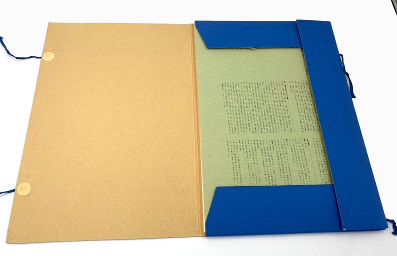May include: An open file folder with a tan cover and a blue spine. Inside, a light green paper holds printed text. The folder is secured with blue string ties and small, round fasteners. The background is white.