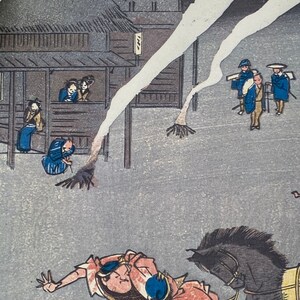 May include: Japanese woodblock print showing a street scene with figures in traditional dress. A man on horseback is in the foreground, with buildings and other figures in the background. The print uses a muted colour palette with shades of grey, blue, and brown.