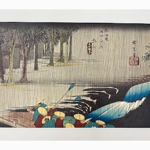 May include: Japanese woodblock print depicting a rainy landscape with figures in boats. The artwork features a waterfall, trees, and traditional Japanese characters. The color palette includes blues, greens, and browns, creating a serene and atmospheric scene.