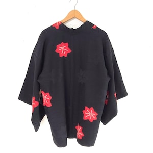 Puede incluir: Kimono negro con bordado floral rojo. El kimono es de estilo japonés tradicional con cuello ancho y mangas largas.
