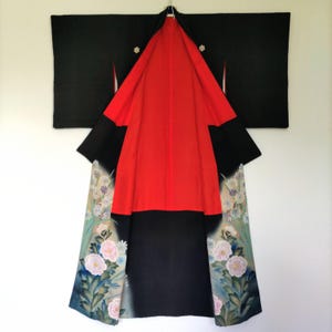 May include: A traditional Japanese kimono, primarily black with a vibrant red interior. The sleeves and lower portion feature floral patterns in shades of pink, blue, and green. The kimono is displayed open, showcasing its intricate design and craftsmanship.