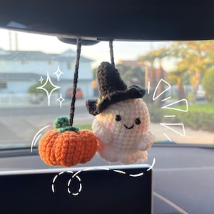 May include: Crocheted Halloween car charm featuring a smiling ghost wearing a black witch hat and an orange pumpkin. The ghost has rosy cheeks and is suspended by a black string. A festive, handmade decoration.