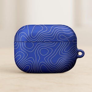 May include: A blue AirPod case with a white topographic map design. The case has a rounded rectangular shape with a small loop on the side. The design features flowing, curved lines across the surface.