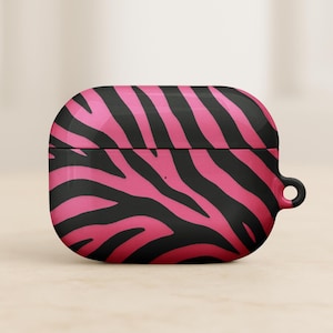 May include: A black and pink zebra-striped AirPod case. The case is a rounded rectangle with a hinged lid and a small loop on the side. The zebra stripes are a vibrant pink against a black background.