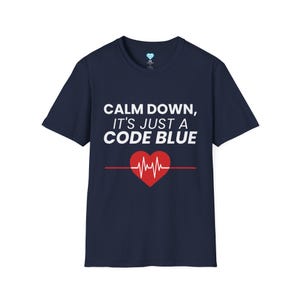 May include: Navy blue t-shirt with the text "CALM DOWN, IT'S JUST A CODE BLUE" in white. A red heart with a heartbeat graphic is below the text. The shirt is a crew neck style.