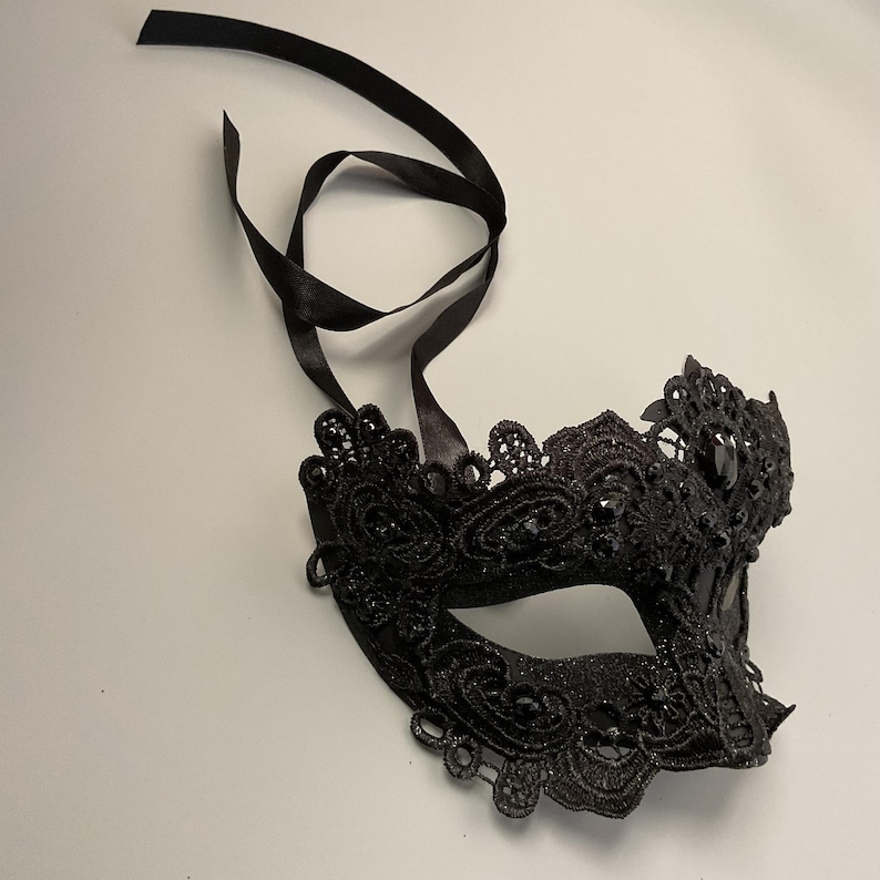 May include: A black lace masquerade mask with a floral design and sparkling accents. The mask has a satin ribbon for tying and is suitable for a costume party or formal event.