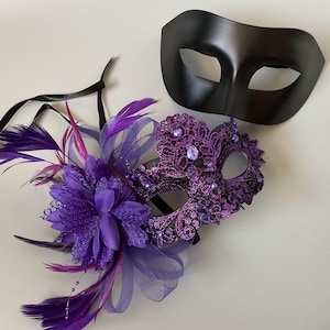 May include: Two masquerade masks. One is a solid black eye mask. The other is a purple lace mask with jewel accents and a floral and feather embellishment. The masks are for a costume or party.