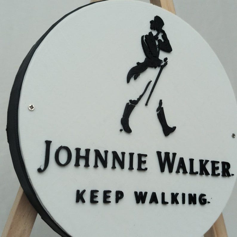 May include: A round white sign with a black border features the Johnnie Walker logo and text. The logo is a black silhouette of a man walking with a cane. The text reads "JOHNNIE WALKER" and "KEEP WALKING."