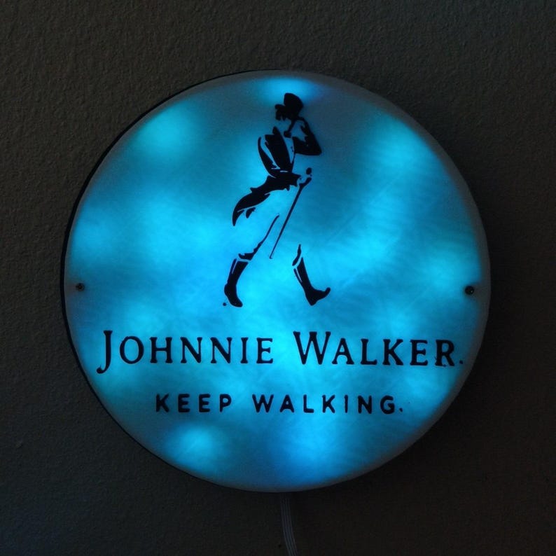 May include: A round, illuminated sign with a blue glow. The sign features the Johnnie Walker logo, a silhouette of a man walking with a cane, and the text "JOHNNIE WALKER. KEEP WALKING."