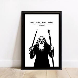 Può includere: Stampa incorniciata in bianco e nero con un'illustrazione di Gandalf de Il Signore degli Anelli. L'immagine mostra Gandalf che tiene una spada e un bastone con la citazione "YOU... SHALL NOT... PASS!" e il nome "-GANDALF".