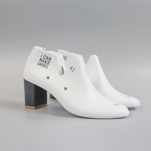 May include: A pair of white shoe lasts with a black heel. The left shoe last has the text "I CAN MAKE SHOES" printed on the side. The right shoe last has the number "41" printed on the side.
