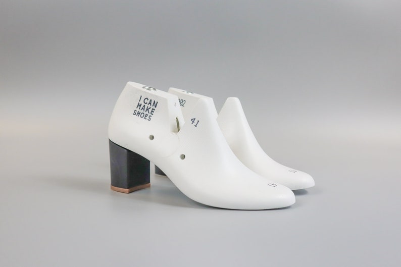 May include: A pair of white shoe lasts with a black heel. The left shoe last has the text "I CAN MAKE SHOES" printed on the side. The right shoe last has the number "41" printed on the side.