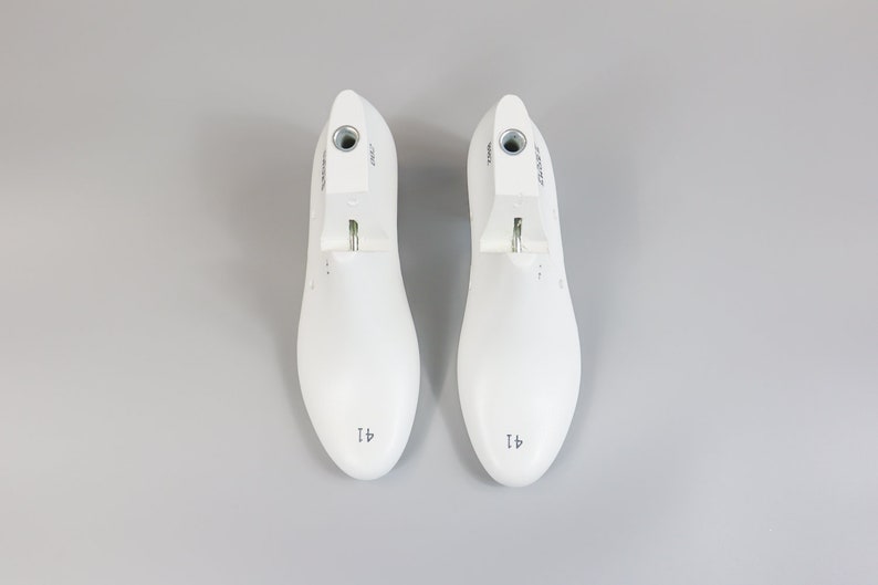 May include: A pair of white shoe trees with a metal spring mechanism. The shoe trees are labeled "41" and have a round toe shape.