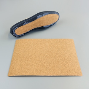 May include: A cork insole and a navy blue shoe sole with a cork footbed are displayed on a gray surface. The insole is rectangular and has a natural, light brown color. The shoe sole is dark blue with a light brown cork footbed.