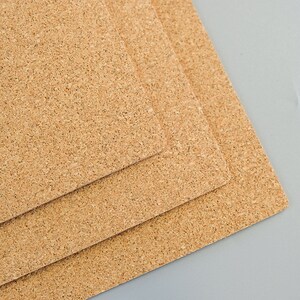 May include: Three rectangular cork boards, each with a natural, textured surface. The boards are stacked, with the top one slightly offset, revealing the edges of the layers below. The cork has a light brown color.