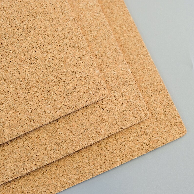 May include: Three rectangular cork boards, each with a natural, textured surface. The boards are stacked, with the top one slightly offset, revealing the edges of the layers below. The cork has a light brown color.