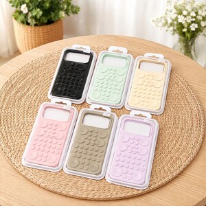 May include: A collection of colorful phone cases in a variety of pastel shades, including black, mint green, yellow, pink, taupe, and lavender. Each case features a textured design and is displayed in a clear plastic package.