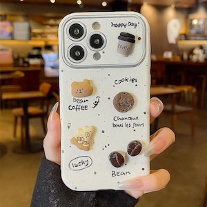 May include: White phone case with a coffee and cookie theme. The case features 3D embellishments of a coffee cup, bear, cookies, and coffee beans. Text includes "happy day!", "cookies", "lucky", and "Bean Coffee".