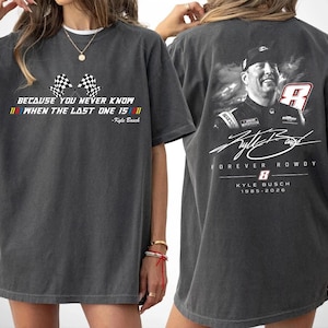 May include: Dark gray t-shirt featuring a racing theme. The front displays checkered flags and text: "BECAUSE YOU NEVER KNOW WHEN THE LAST ONE IS." The back has a portrait of Kyle Busch, the number 8, and the text "FOREVER ROWDY."