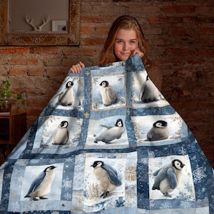 Puede incluir: Una manta azul y blanca con temática de pingüinos. La manta presenta un patrón de cuadrícula con ilustraciones de pingüinos en un paisaje nevado. La paleta de colores incluye tonos de azul, blanco y gris, con acentos de copos de nieve. La manta es de material suave.