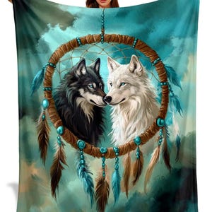 May include: A turquoise and teal blanket featuring a dreamcatcher design with two wolves. One wolf is black with blue eyes, the other is white with blue eyes. The dreamcatcher has brown feathers and turquoise beads.